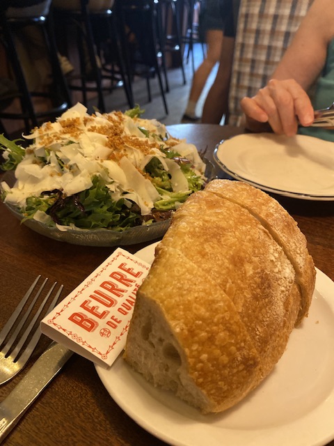 A photo of a loaf of bread, butter, and a large salad.